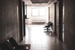 A dimly lit empty corridor with chairs and a waiting area, conveying a quiet atmosphere.