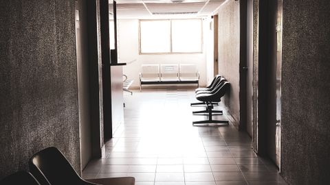 A dimly lit empty corridor with chairs and a waiting area, conveying a quiet atmosphere.