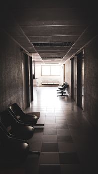 A dimly lit empty corridor with chairs and a waiting area, conveying a quiet atmosphere.