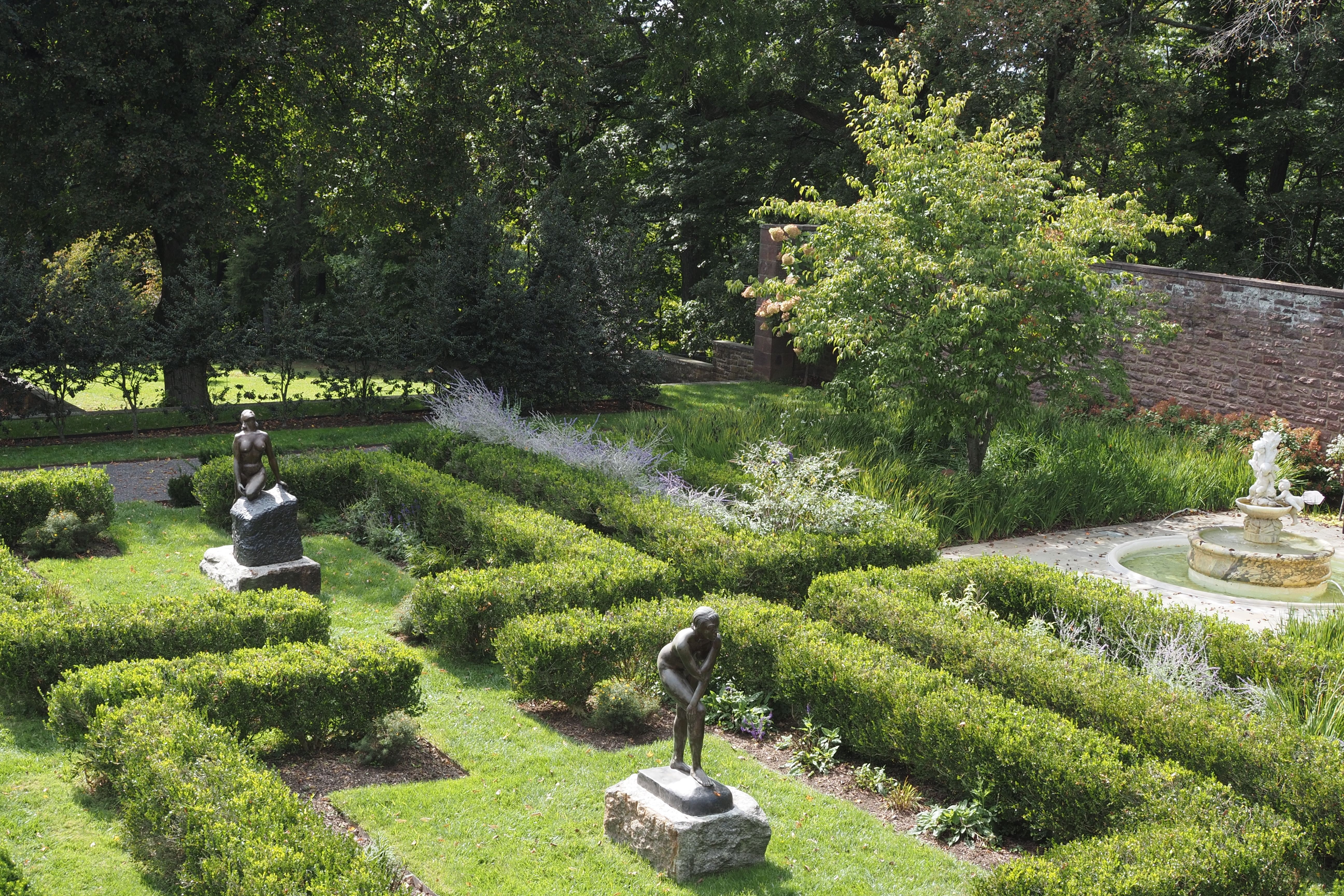Beautiful garden in Newtown, PA with statues, hedges, and a fountain on a sunny day.