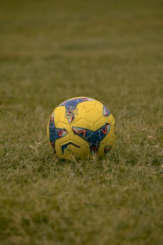 Close-up of a colorful yellow soccer ball on a green grass field, sports theme.