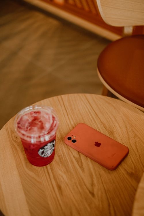 Free A refreshing iced beverage in a disposable cup next to a smartphone on a wooden table, captured indoors. Stock Photo