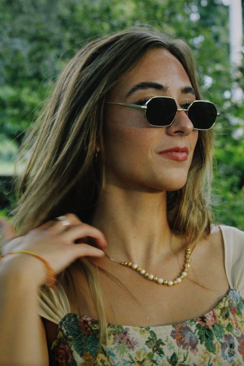 Free Portrait of a stylish woman wearing sunglasses and a floral dress, showcasing modern fashion. Stock Photo
