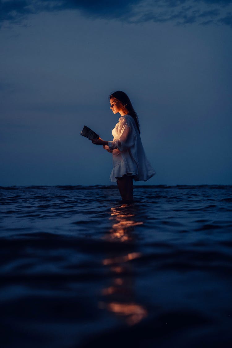 Woman Standing In Water In Evening And Reading Book