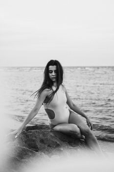 Artistic black and white photo of a woman sitting on coastal rocks.