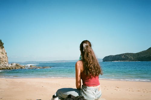 Back View of Woman Sitting on Beach on Sea Shore