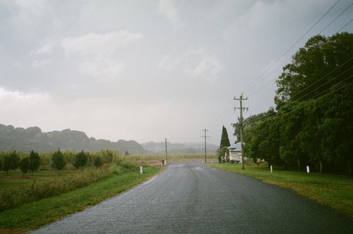 Free A tranquil rural road in the countryside surrounded by lush greenery and overcast sky. Stock Photo