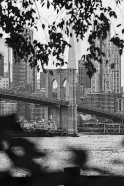 Monochrome view of Brooklyn Bridge framing New York City skyscrapers.