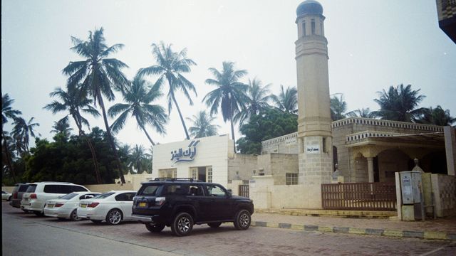 Exterior view of a mosque in Salalah, Oman, with palm trees and parked cars in the background. — lounges at Salalah Airport