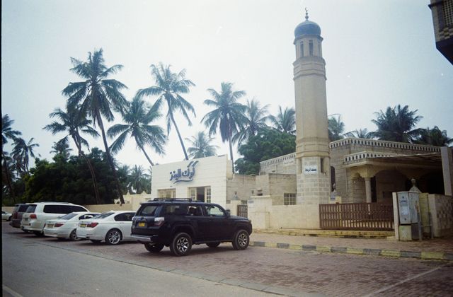 Exterior view of a mosque in Salalah, Oman, with palm trees and parked cars in the background. — arriving in Salalah