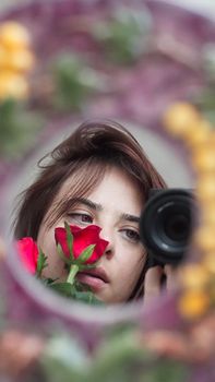 Portrait of a woman with brown hair, holding a red rose, reflected in a mirror.