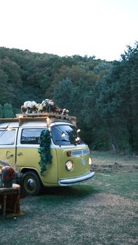 A charming yellow vintage Volkswagen van adorned with flowers in a serene forest landscape.
