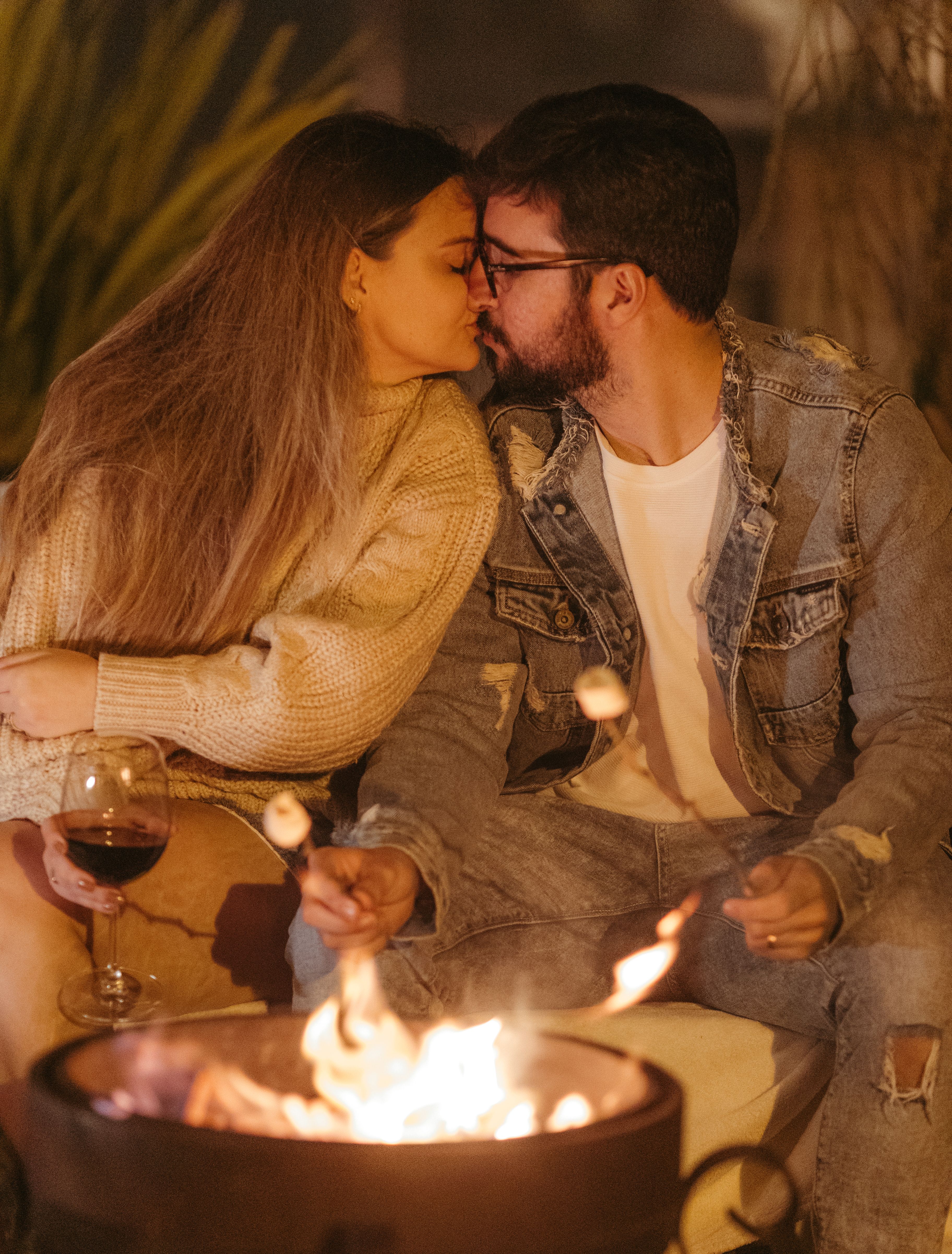 Cozy couple sitting by campfire, toasting marshmallows, enjoying intimate moment. Perfect for lifestyle and romance themes.