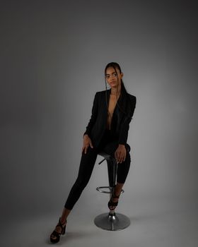 A young woman sits confidently on a bar stool in a stylish studio shoot.