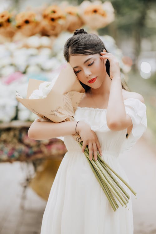 Young Woman Wearing a White Off the Shoulder Summer Dress Holding a Bouquet of Flowers