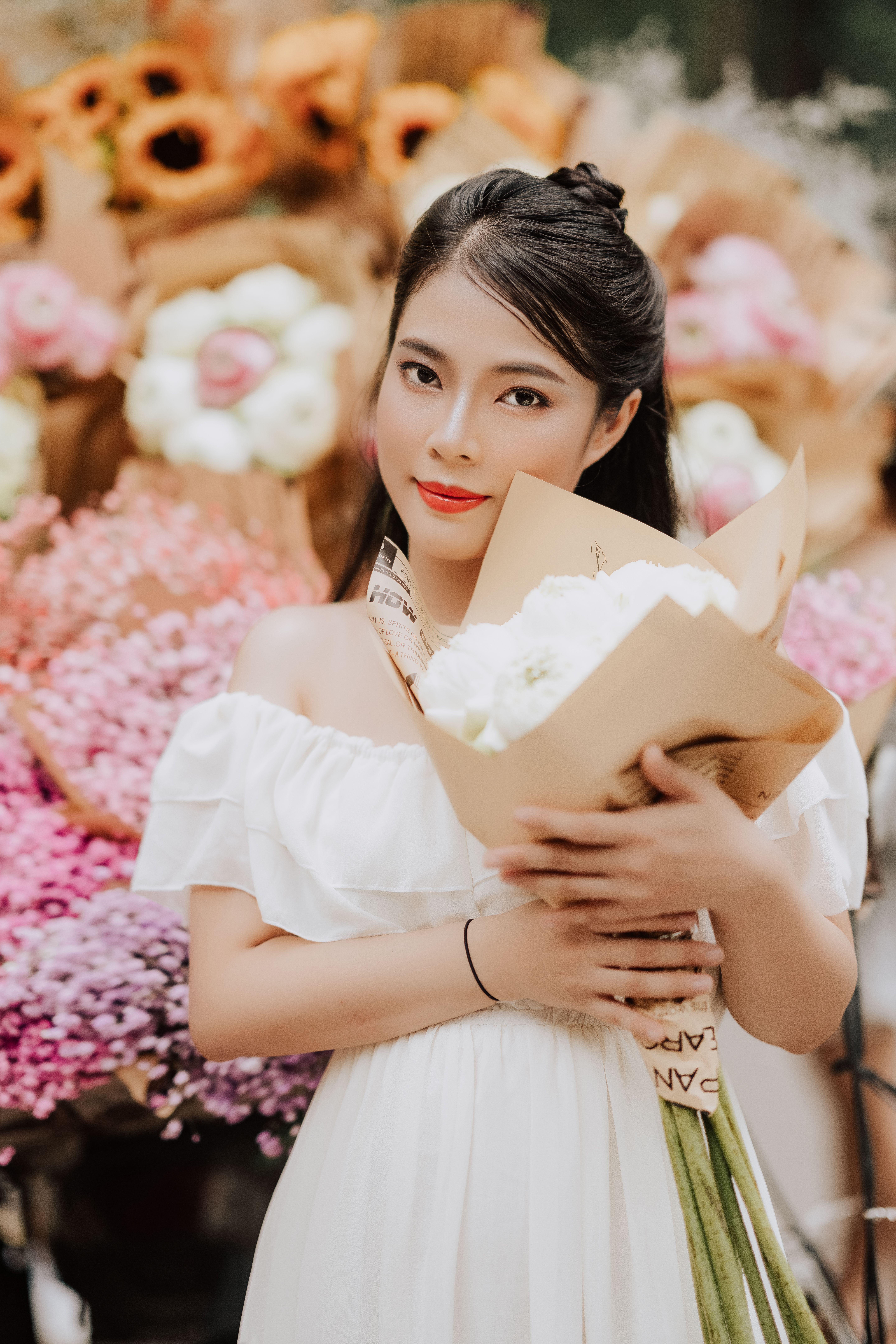 A young woman in a white dress gracefully holding a bouquet of flowers with a vibrant floral backgro