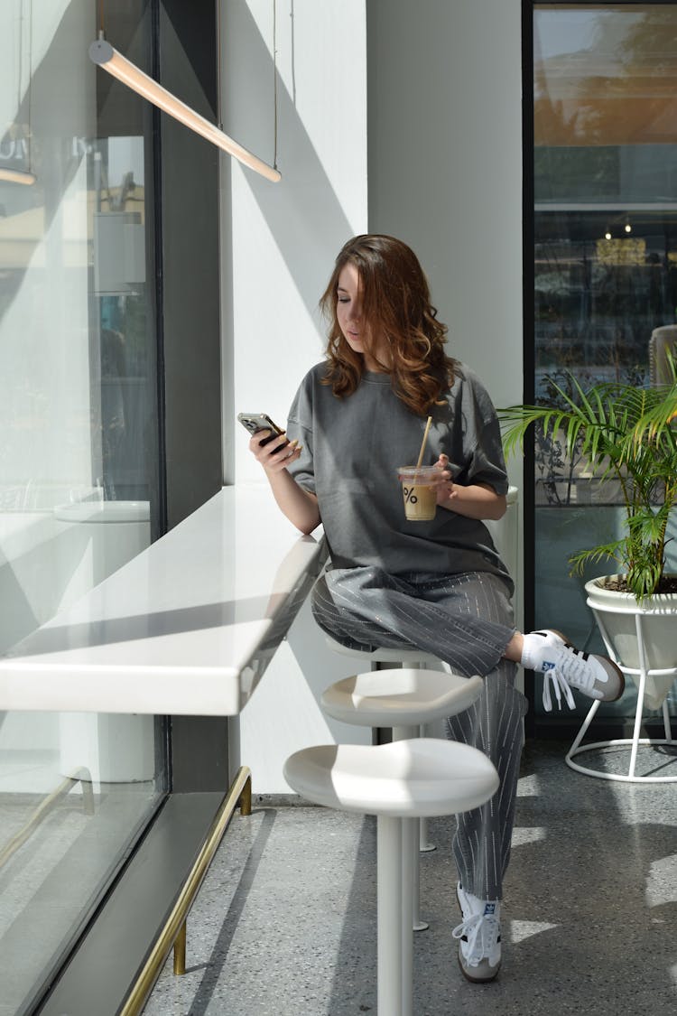 Woman Sitting With Smartphone By Window In Cafe