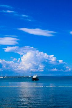 A tranquil maritime scene featuring a yacht under a vibrant blue sky with fluffy clouds.