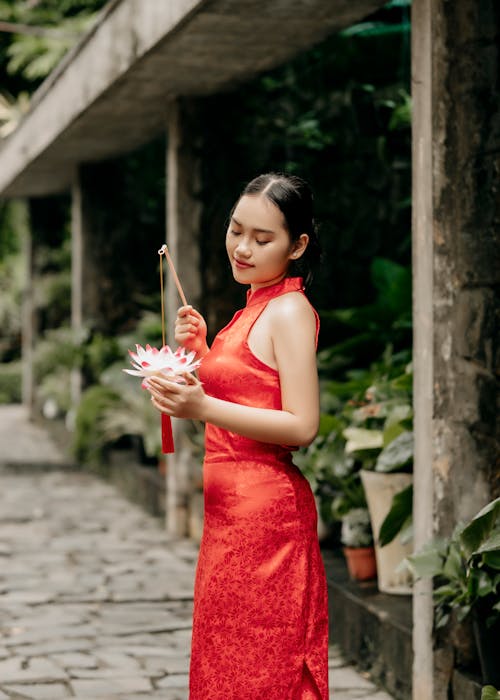 Young Woman in a Red Dress Standing Outside and Holding a Lotus Flower