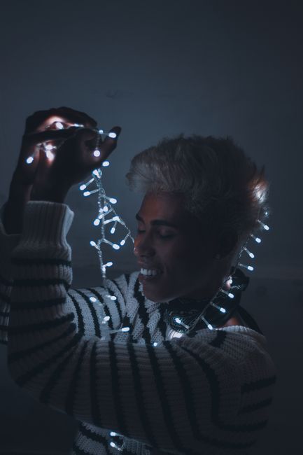 Smiling man with fairy lights in a cozy sweater, creating a warm glow.
