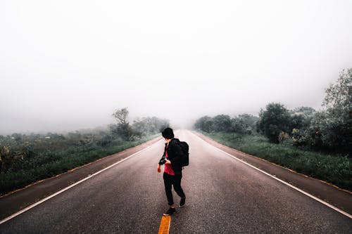 Free Person Waling in the Middle of Road in Between Grass Field Under White Skies Stock Photo