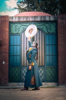 Woman in traditional attire with painted face celebrating Dia de Muertos, posing outdoors.
