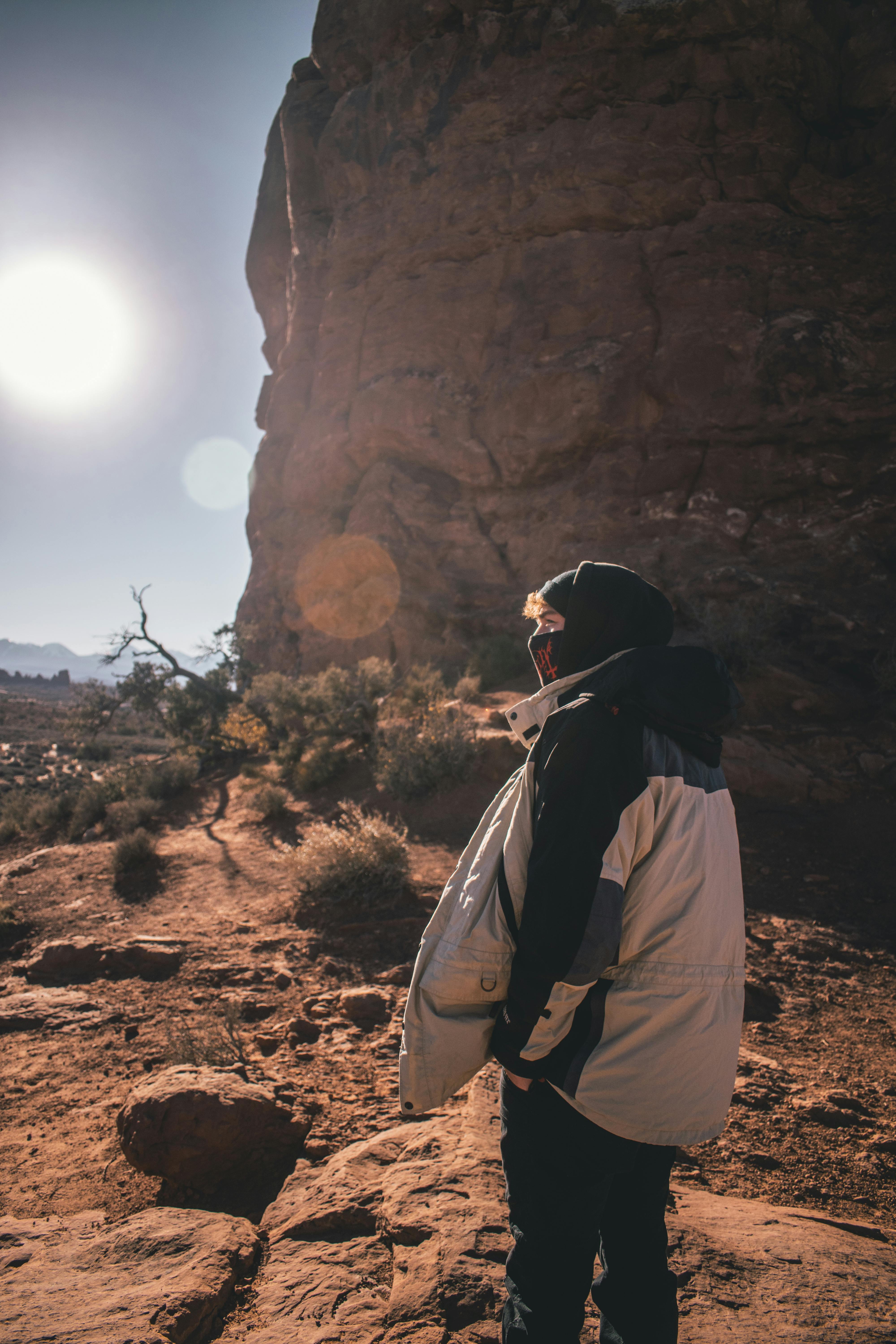 一个人穿着冬季夹克，站在阳光普照的岩石沙漠中，可能正在探索荒野