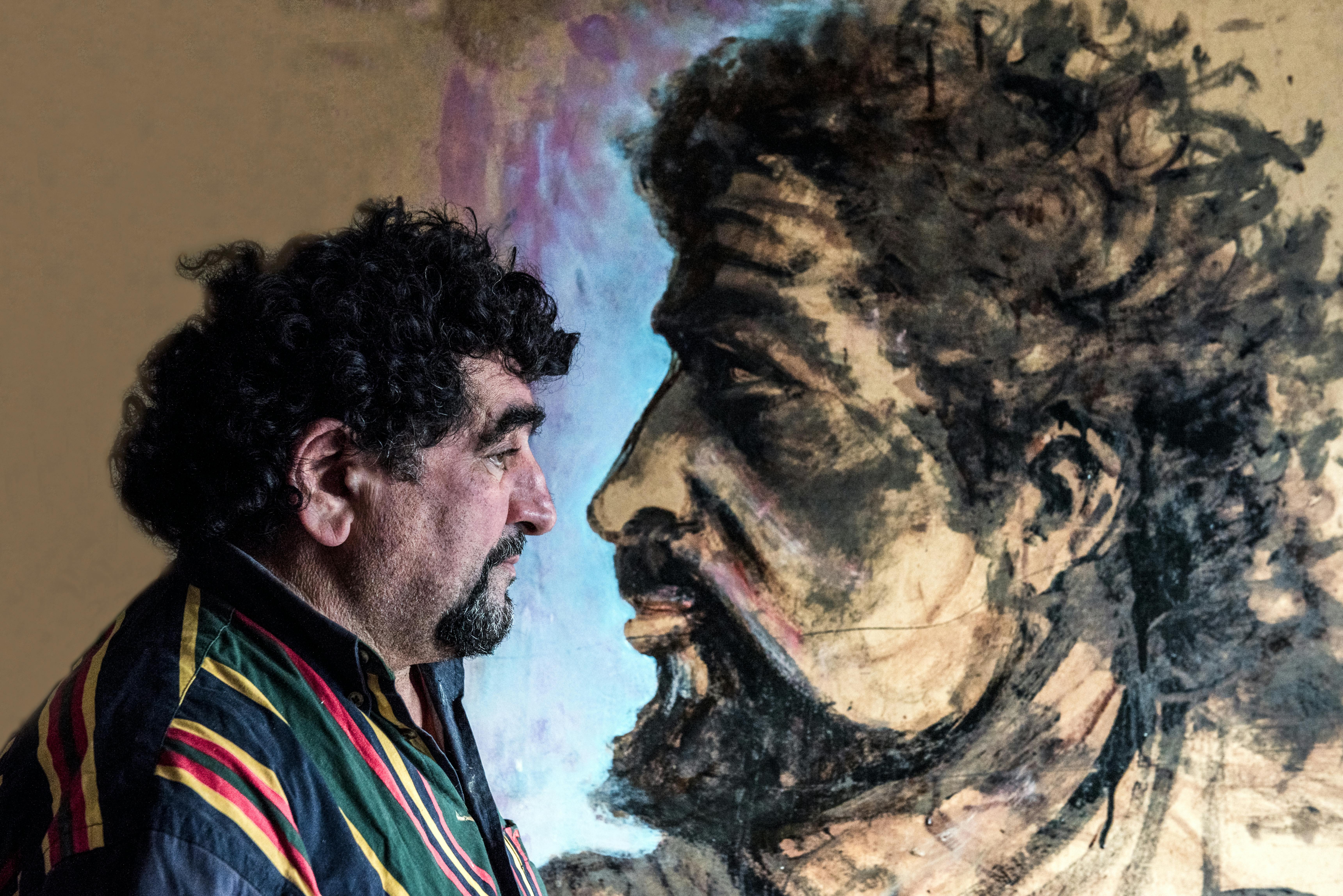 Side profile of a man with beard looking at an artistic painted portrait on a wall.
