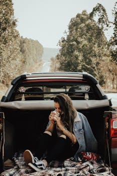 一名年轻女子在树木环绕的风景秀丽道路上，于汽车后备箱里享受着宁静的时刻