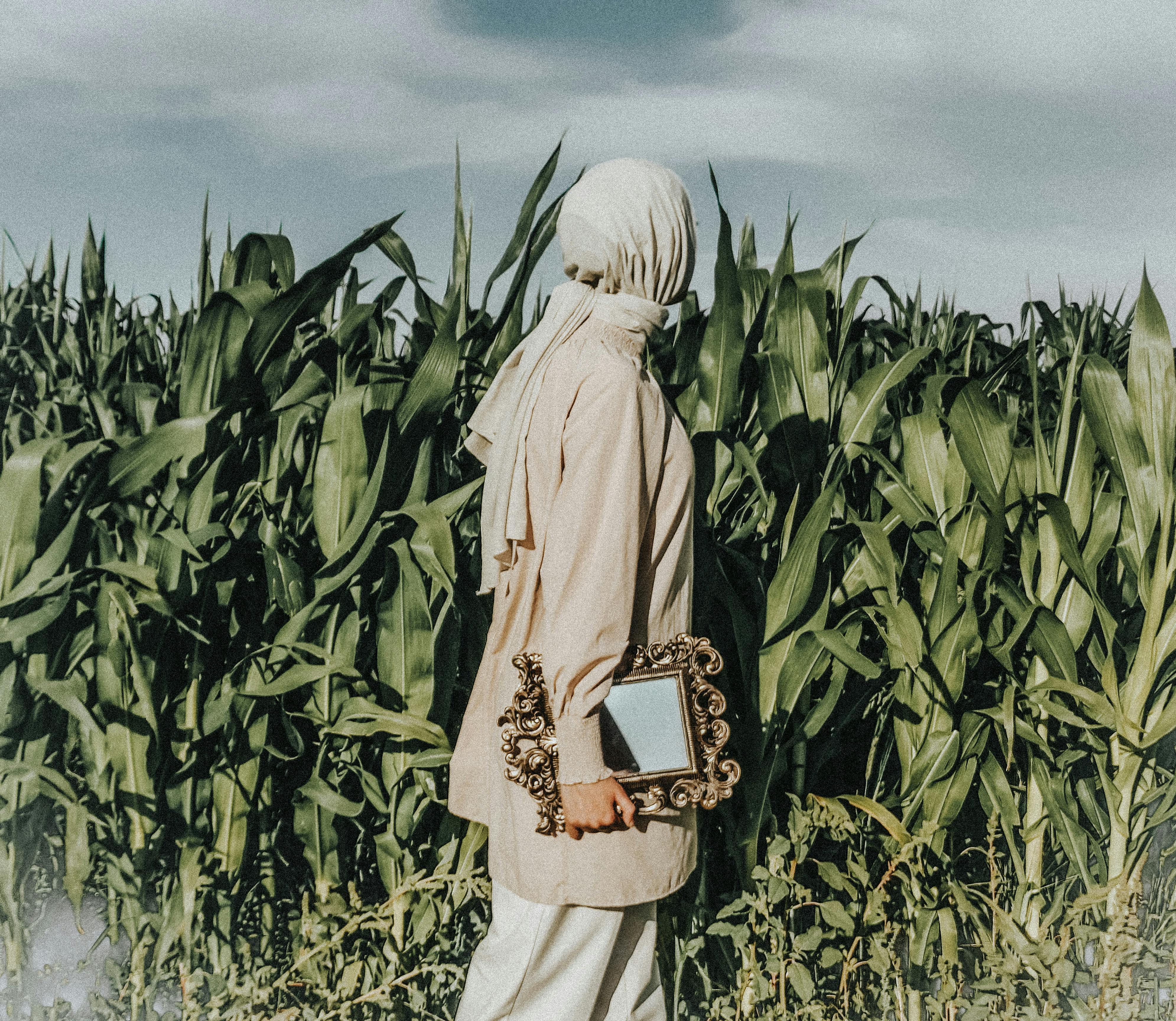 A woman in a cornfield holding a vintage mirror during summer, creating a rustic fashion scene.