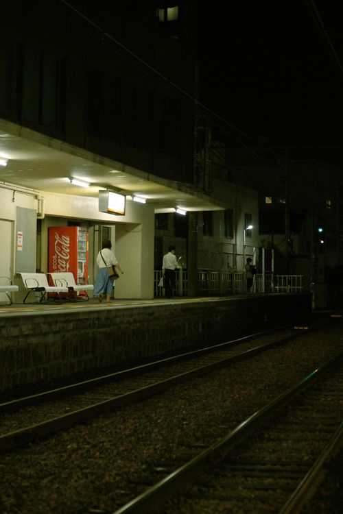 Free People waiting at a dimly lit railway station platform at night, capturing a tranquil urban scene. Stock Photo