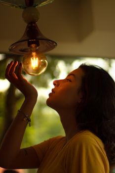 A woman thoughtfully gazes at an illuminated light bulb, creating a warm and introspective atmosphere.