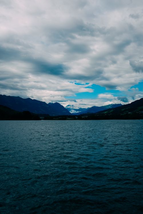 Free Dramatic cloudy sky over a beautiful mountain range and clear blue waters, creating a serene nature scene. Stock Photo
