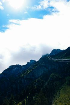 Cable car crossing mountainous terrain under a bright sky with clouds.