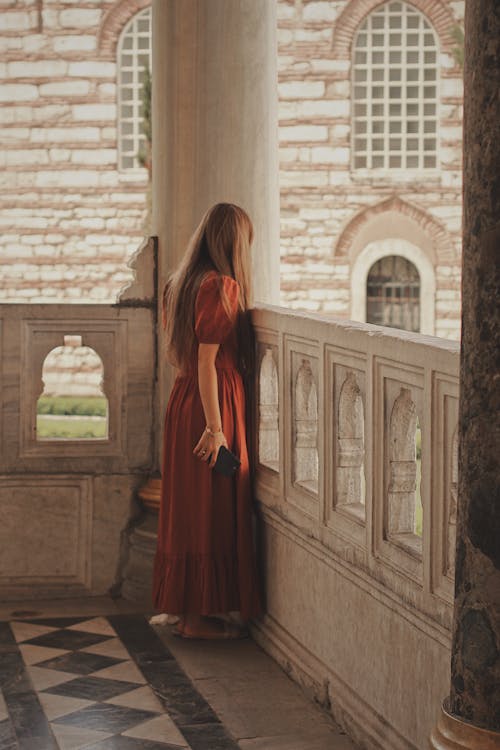 Woman in Red Dress Standing in Corner of Marble Balcony