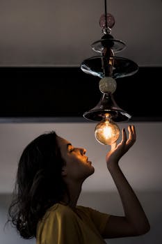 一个女人凝视着设计独特的灯具中发光的灯泡，神情专注，营造出喜怒无常的氛围