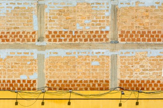 Abstract view of an industrial brick wall with exposed electrical wires and yellow base.