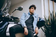 一位穿着牛仔夹克的年轻人自信地倚着摩托车摆姿势，展现出都市现代风格