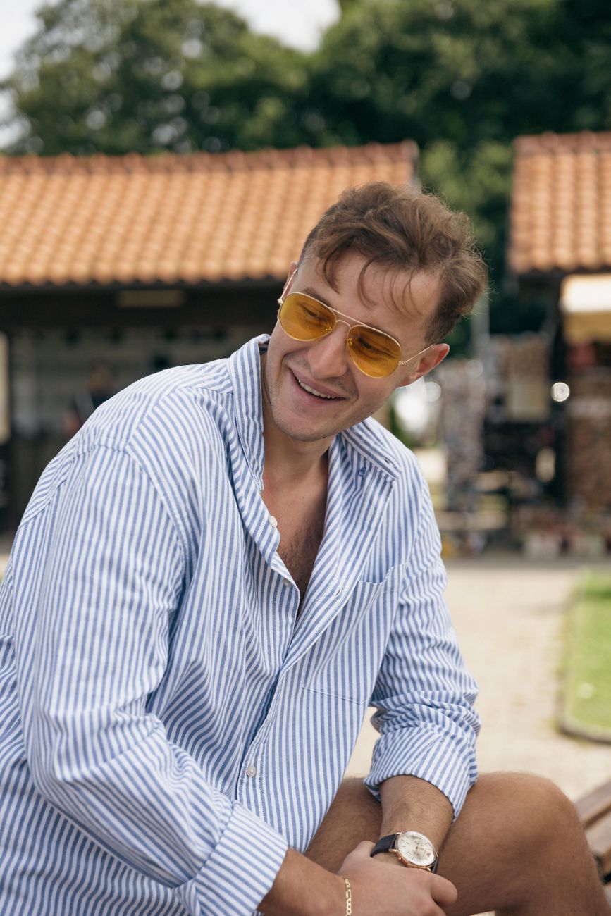 A cheerful man in a striped shirt outdoors, closer to everyday summer dressing than country-club cosplay.