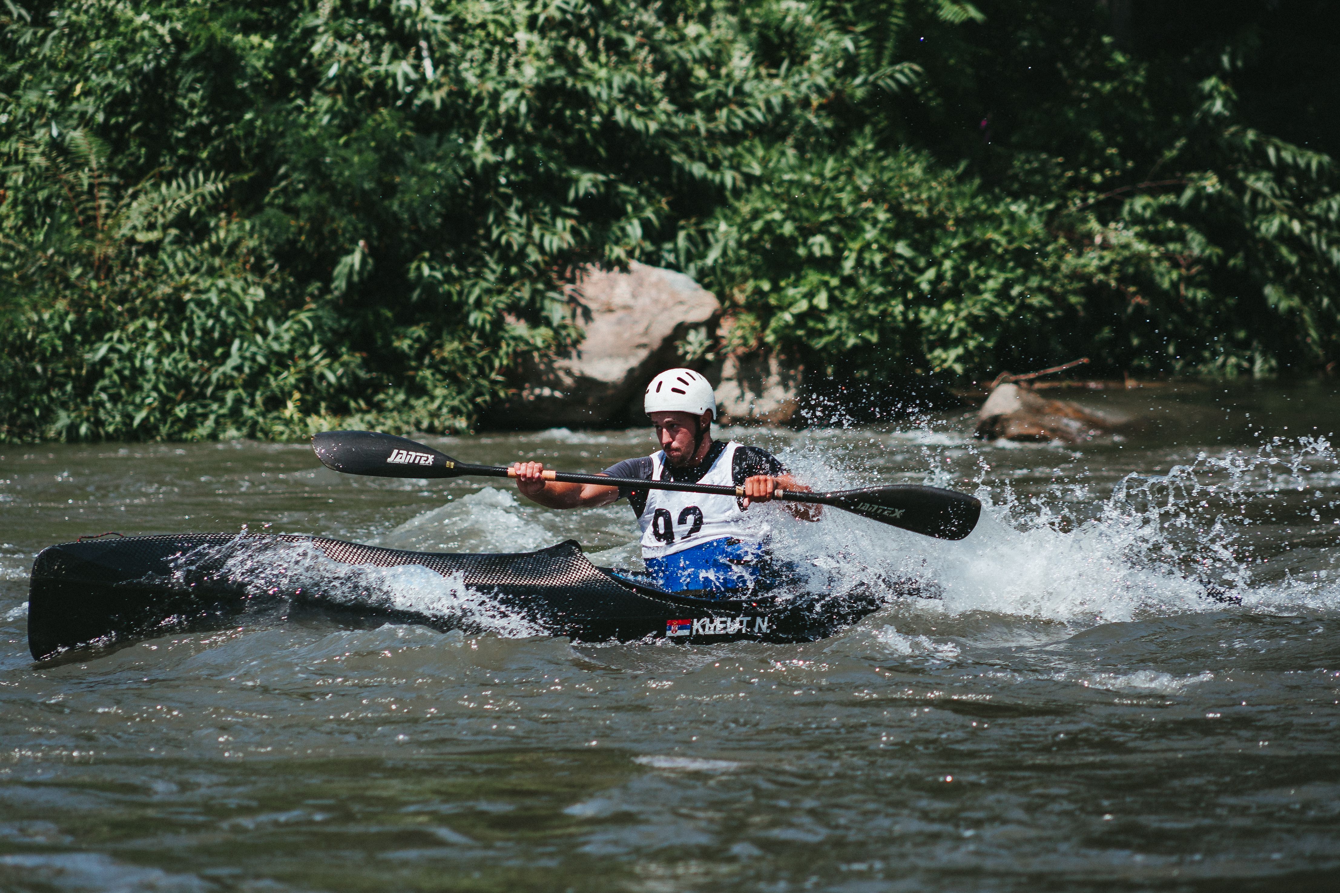 An adult male kayaking through river rapids with splashing water, showing adventure and sport.