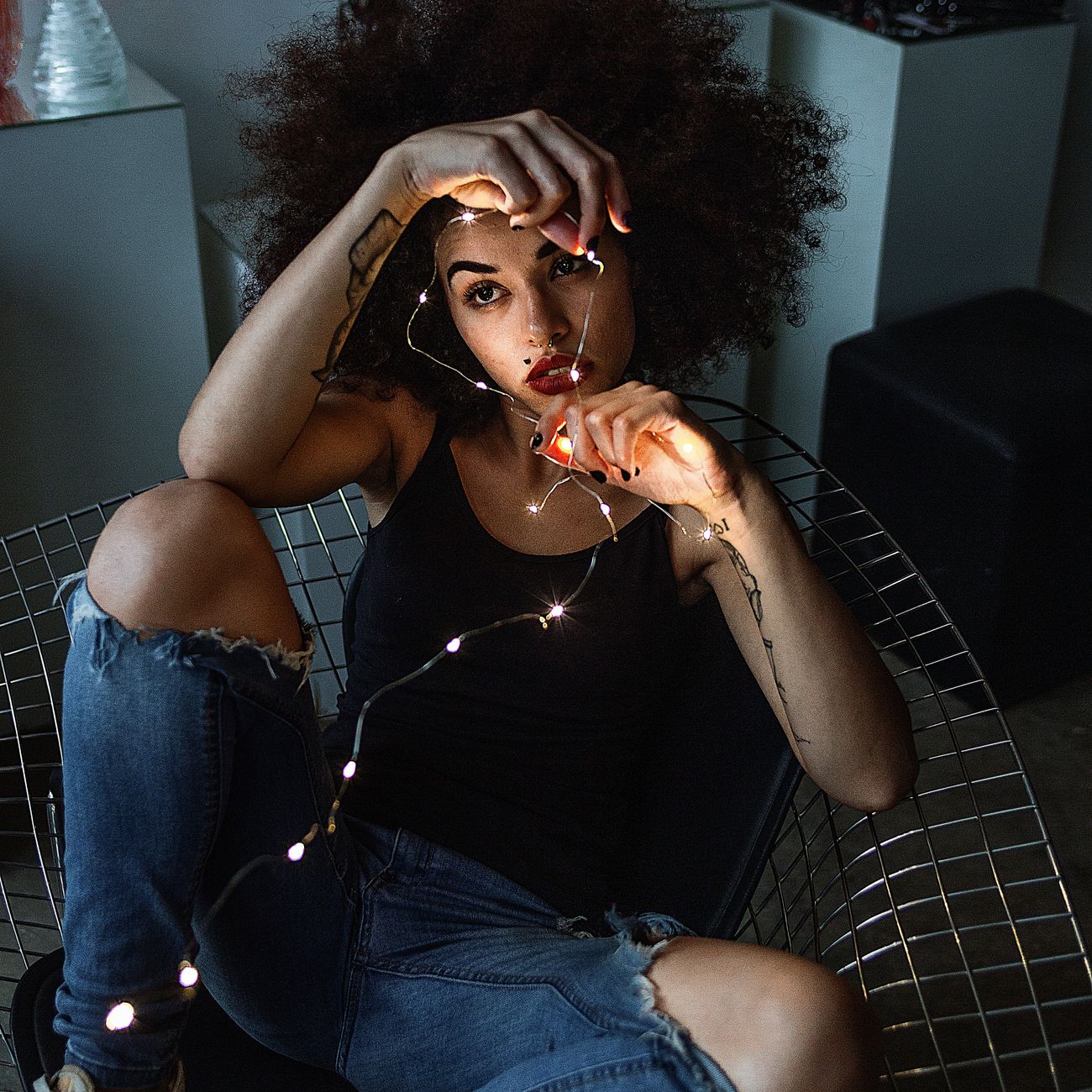 A woman sitting indoors, creatively illuminated by string lights, creating a warm and artistic scene.