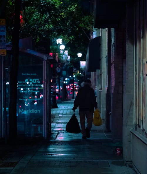 Person with Bags Walking Down Sidewalk in Evening