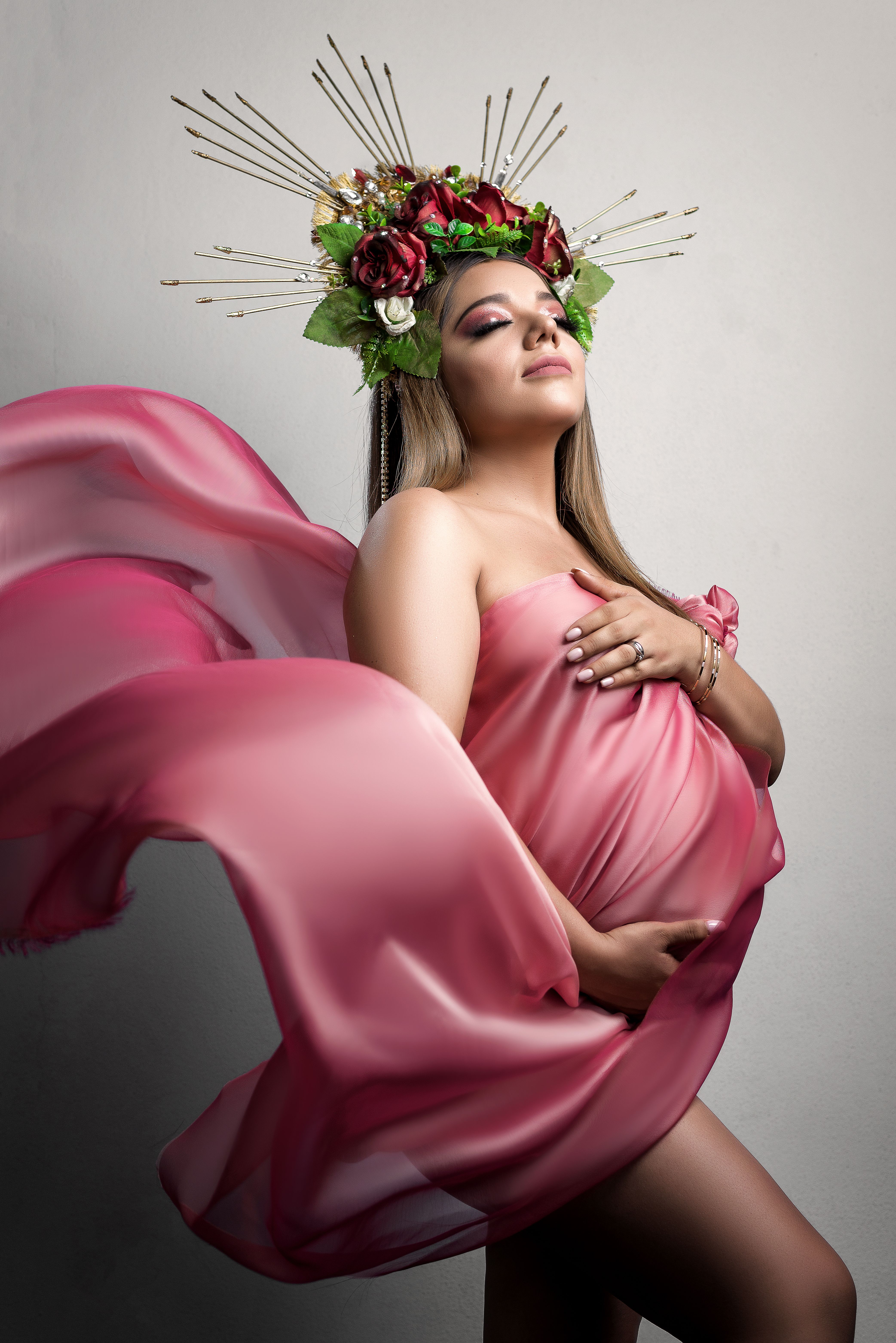 Stunning pregnant woman in pink fabric with flowers, exuding grace and beauty.