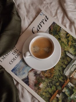 A warm cup of coffee placed on an art magazine in a cozy indoor setting.