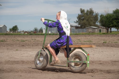 Girl in Purple Dress Riding on Handmade Scooter