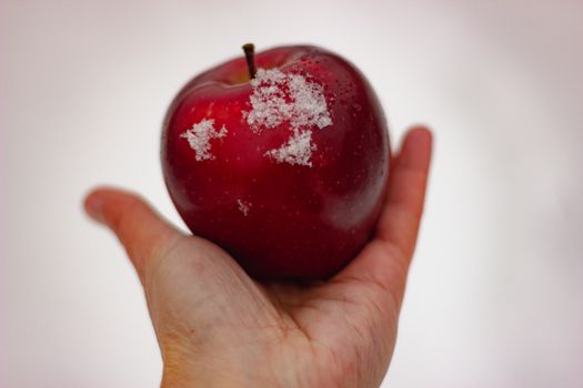 A close-up of a hand holding a red apple with frost on a white background.
