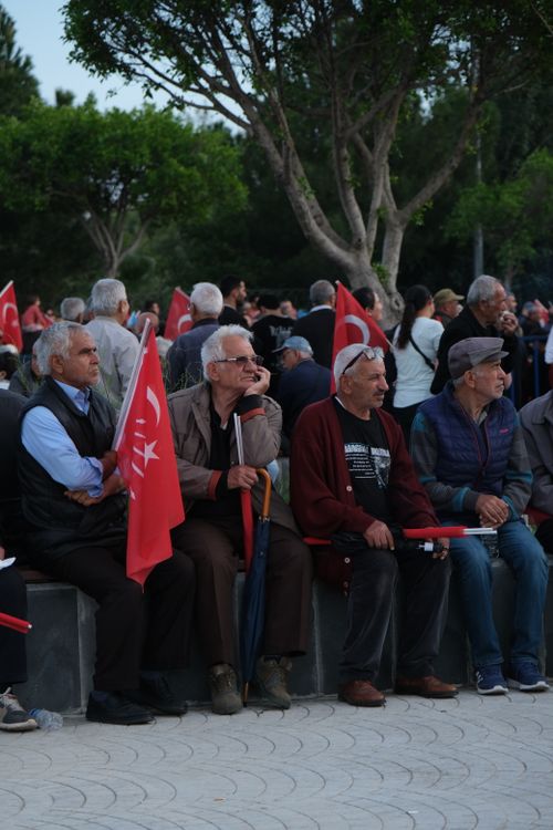 Free A group of elderly men holding Turkish flags sit in an outdoor city square during a public rally or gathering. Stock Photo