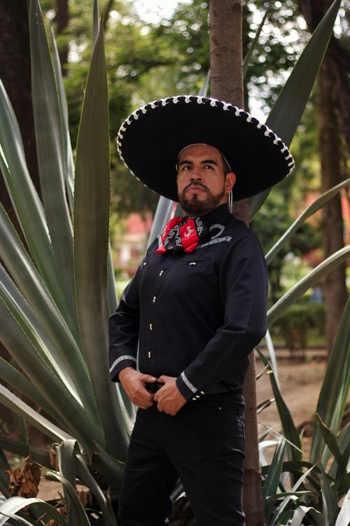 Free Portrait of a man in traditional Mexican charro attire and sombrero amidst lush greenery. Stock Photo