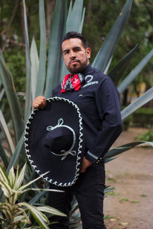 Free Portrait of a man in traditional Mexican clothing holding a sombrero in an outdoor setting. Stock Photo