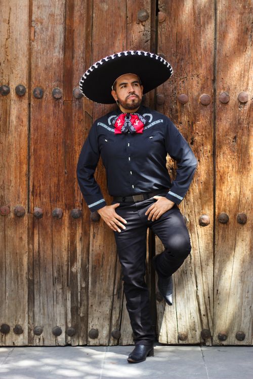Free Portrait of a Mexican man in traditional charro clothing posing against a rustic wooden wall. Stock Photo